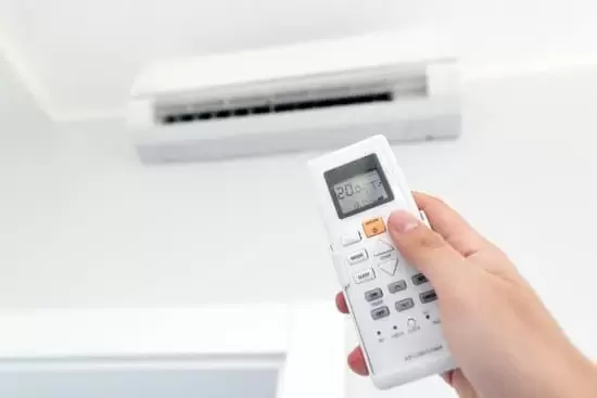 Indoor residential wall mounted air conditioning unit and hand holding a remote control pointing it at the AC unit